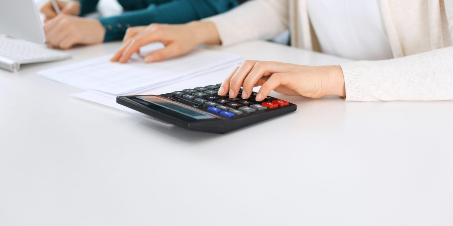 Accountant checking financial statement or counting by calculator income for tax form, hands close-up. Business woman sitting and working with colleague at the desk in office. Audit concept.